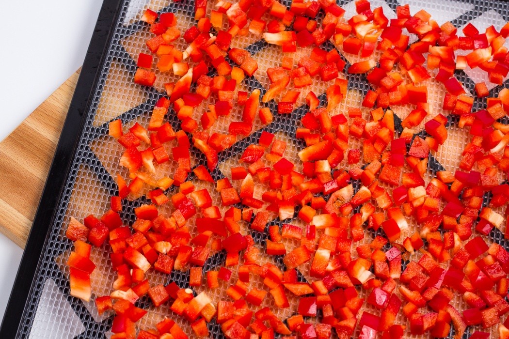 Spread red bell peppers on a dehydrator tray, avoid overlapping as they may stick. diced red bell peppers spread on a dehydrator tray