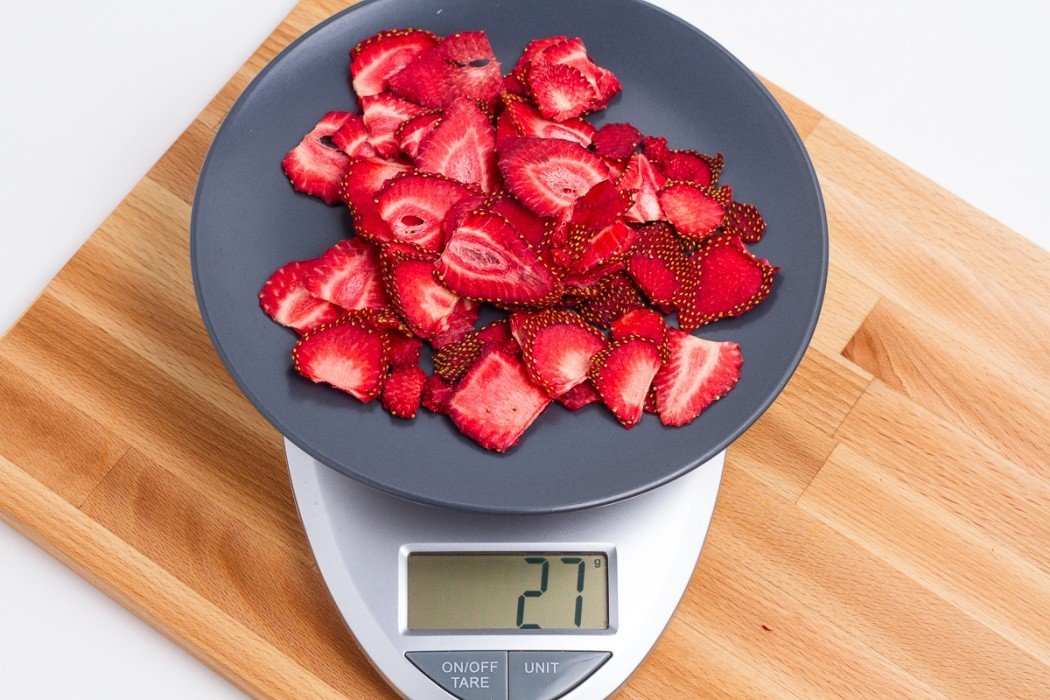 Dried strawberries will be kind of crispy but mostly leathery 27 grams of dried strawberries on a blue plate on a scale
