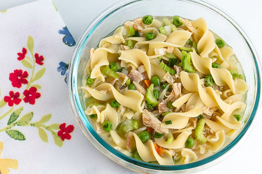 bowl of chicken noodle soup with peas, carrots, celery, and mushrooms