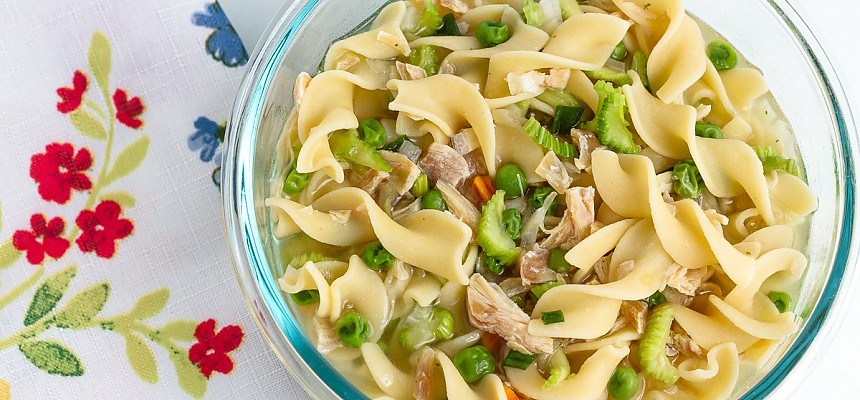 bowl of chicken noodle soup with peas, carrots, celery, and mushrooms