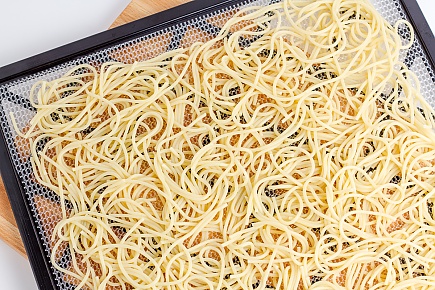 spaghetti noodles spread on a dehydrator tray